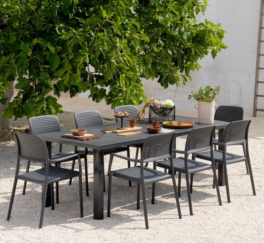 Juego de sillas BORA alrededor de una mesa de comedor en un jardín de construcción moderna.