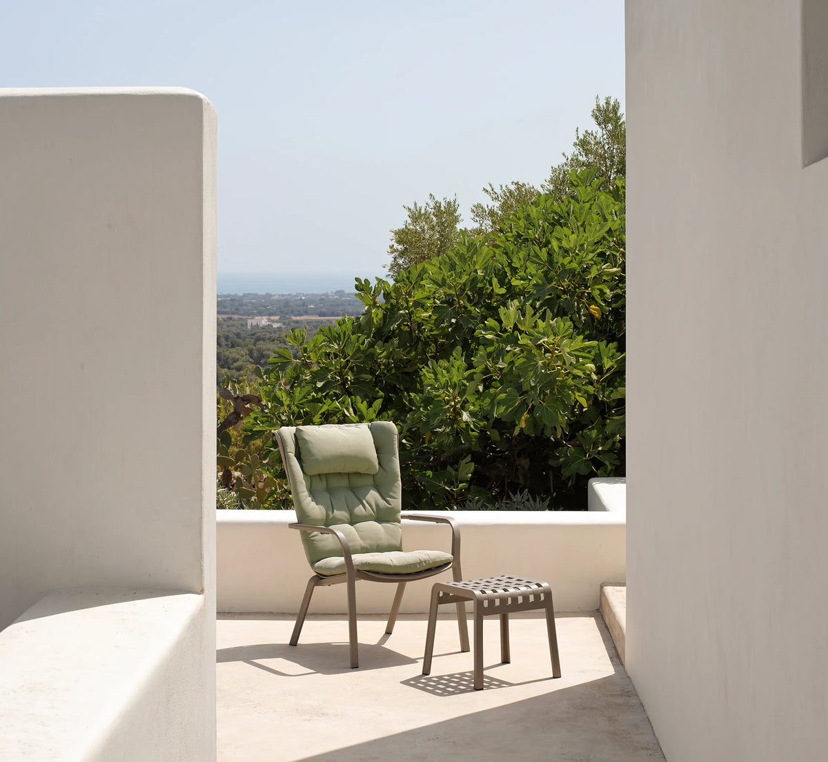 Sillón FOLIO con el reposapiés POGGIO en un jardín moderno, creando un conjunto de relax completo.