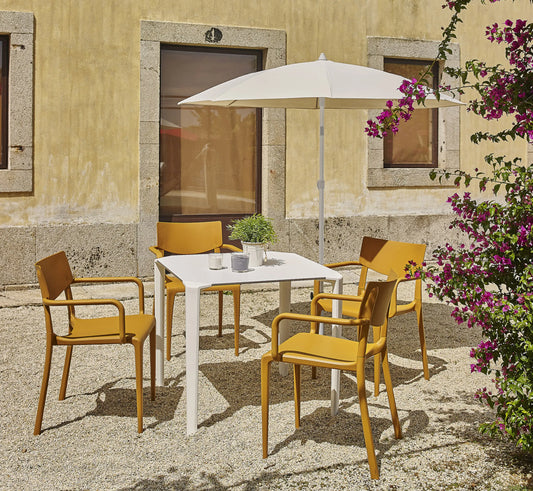 Mesa ONE acompañada de sillas TOWN, creando un comedor de exterior luminoso y de líneas puras en un jardín moderno.