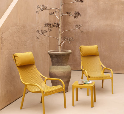 Rincón de relax exterior con la mesa auxiliar NET y sillones a juego, creando una atmósfera de bienestar y lujo silencioso.