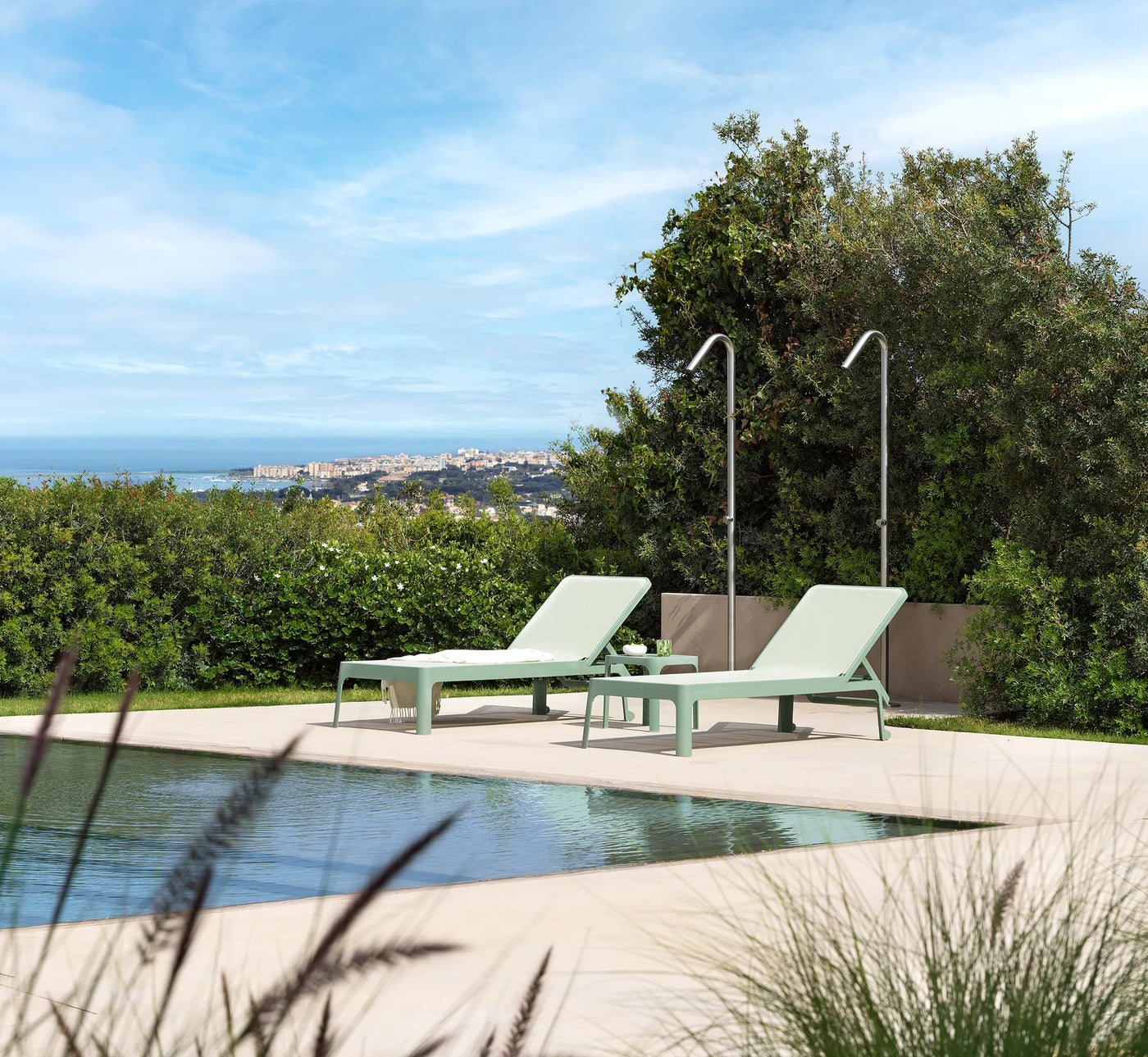 Tumbona PLANO en posición de relax total junto a una piscina desbordante, evocando bienestar y lujo contemporáneo.